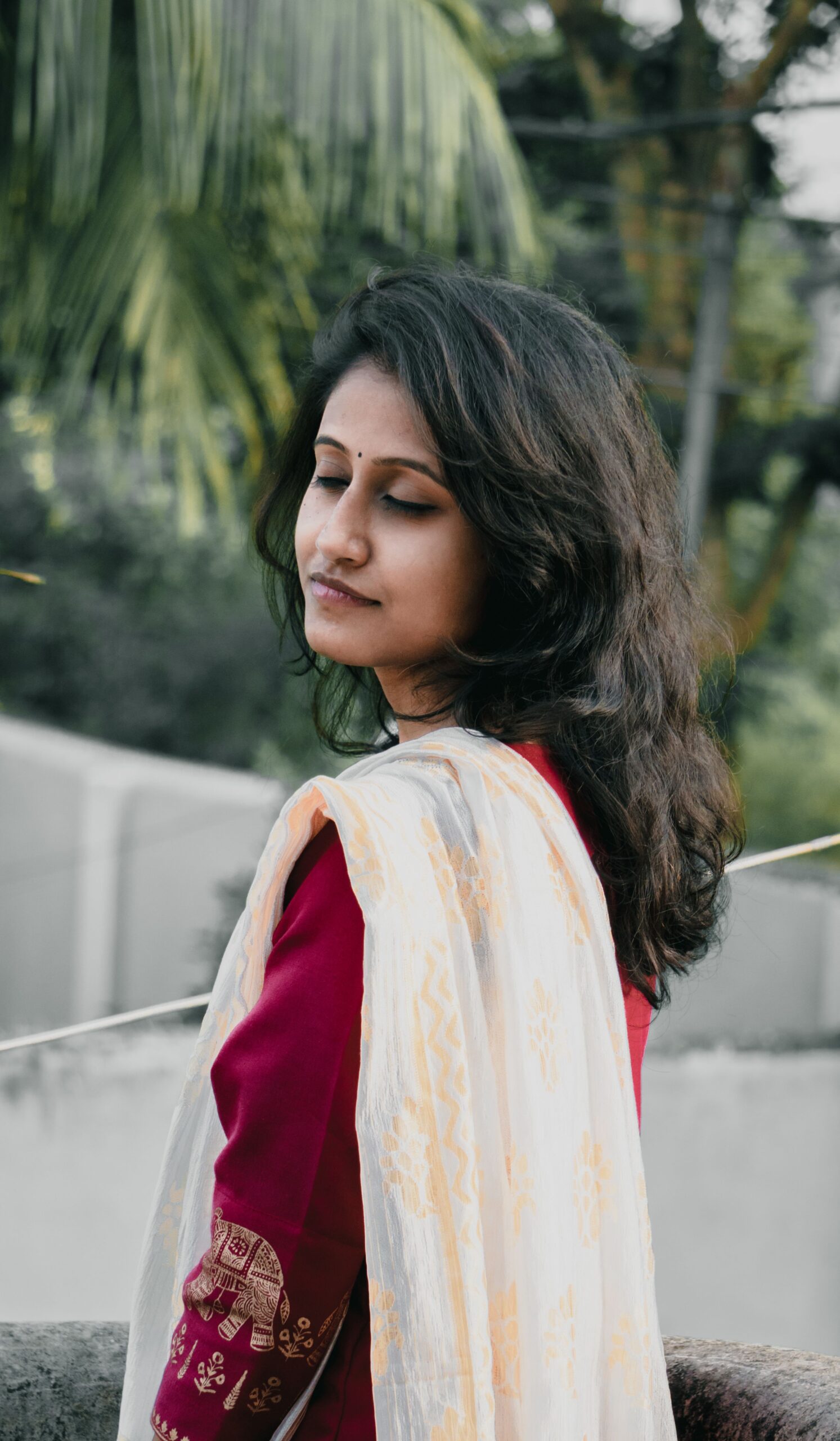 Elegant woman in traditional dress poses outdoors with eyes closed, conveying tranquility.